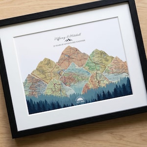 May include: Framed art print featuring a mountain range design made from vintage maps. The artwork includes a forest silhouette, a rising sun, and the text "22 YEARS OF ADVENTURES TOGETHER" and "EST 2004". The frame is black.