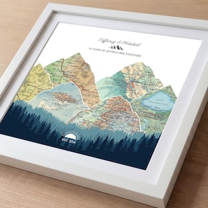 May include: Framed art print featuring a mountain range design composed of vintage map sections. The artwork includes text that reads "Tiffany & Hitchell" and "10 YEARS OF ADVENTURES TOGETHER." A dark blue forest and sun graphic is at the bottom, with "EST. 2016."