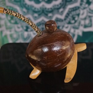 May include: A handcrafted coconut shell pipe with a wooden base and a woven straw stem. The pipe is brown with a small wooden knob on top. The stem is tan, brown, and green.