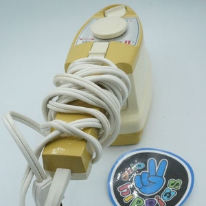 May include: A vintage yellow and white handheld steamer with a white cord wrapped around it. The steamer has a round knob and a label that reads "Steamer II".