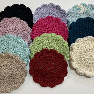 May include: A set of ten crocheted coasters in various colors, including pink, blue, green, white, red, and black. The coasters are all round and have a scalloped edge.