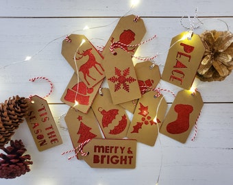 May include: A set of ten brown gift tags with red glitter designs. The designs include a snowflake, a stocking, a Christmas tree, a reindeer, a bell, a holly sprig, an ornament, a deer, and the words "Peace" and "Tis the Season".