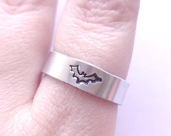 May include: A silver ring with a cutout bat design. The ring is worn on a finger with dark nail polish.
