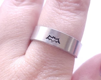 May include: A silver ring with a bat design. The ring is worn on a finger with dark nail polish.