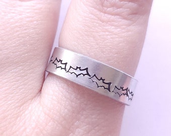 May include: A silver ring with a band of bats etched into the metal.