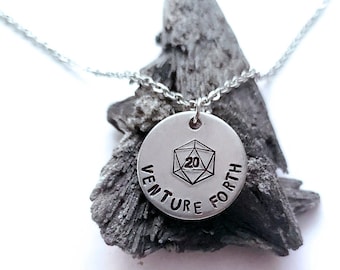 May include: A silver necklace with a round pendant featuring a 20-sided die and the words "Venture Forth".