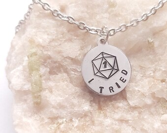 May include: A silver necklace with a round pendant featuring a 20-sided die with the number one and the words "I Tried" around the die.