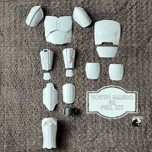 May include: A complete set of white plastic armor pieces for a youth-sized Mandalorian costume. The set includes a chest piece, shoulder pads, arm pieces, leg pieces, and a jetpack. The text "YOUTH MANDO S2 FULL KIT" is printed on a white label.