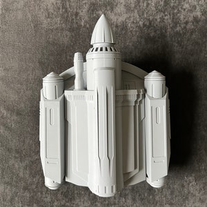 K&ouml;nnte beinhalten: Ein wei&szlig;es, 3D-gedrucktes Modell eines Raumschiffs mit einer spitzen Nase und zwei Seitenfl&uuml;geln. Das Modell hat ein detailliertes Design mit mehreren Paneelen und einer kleinen, zylindrischen Struktur auf der Oberseite.