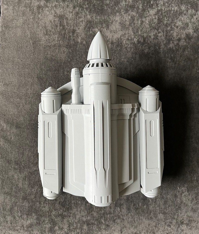 K&ouml;nnte beinhalten: Ein wei&szlig;es, 3D-gedrucktes Modell eines Raumschiffs mit einer spitzen Nase und zwei Seitenfl&uuml;geln. Das Modell hat ein detailliertes Design mit mehreren Paneelen und einer kleinen, zylindrischen Struktur auf der Oberseite.