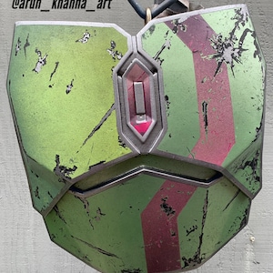 Puede incluir: Una pieza de pecho pintada de verde y rojo para cosplay o disfraz. La pieza de pecho tiene un aspecto desgastado y envejecido. El texto "Finished by: @arun_khanna_art" es visible en la imagen.