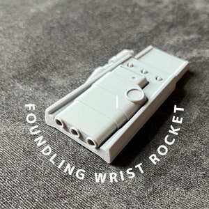 May include: A gray plastic wrist rocket with three holes on the side and the words "Foundling Wrist Rocket" printed on the bottom.