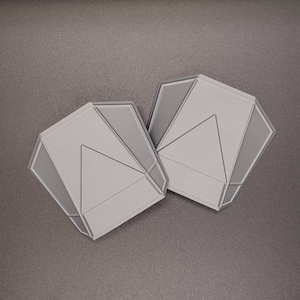 May include: Two gray geometric-shaped silicone molds with a triangular design. The molds are made of flexible silicone and are designed for making soap, candles, or other crafts.