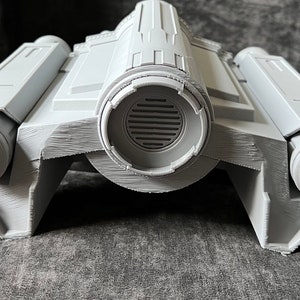 K&ouml;nnte beinhalten: Ein graues 3D-gedrucktes Modell eines Raumschiffs mit zwei Triebwerken an jeder Seite und einer gro&szlig;en runden L&uuml;ftungs&ouml;ffnung in der Mitte.