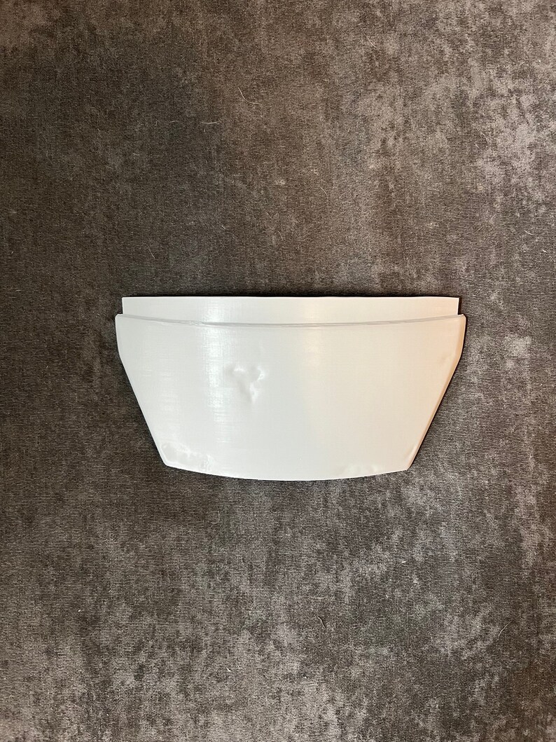 May include: A white, geometric-shaped planter with a curved bottom and straight sides. The planter is made of a solid material and has a smooth, matte finish. The design is modern and minimalist, suitable for small plants.