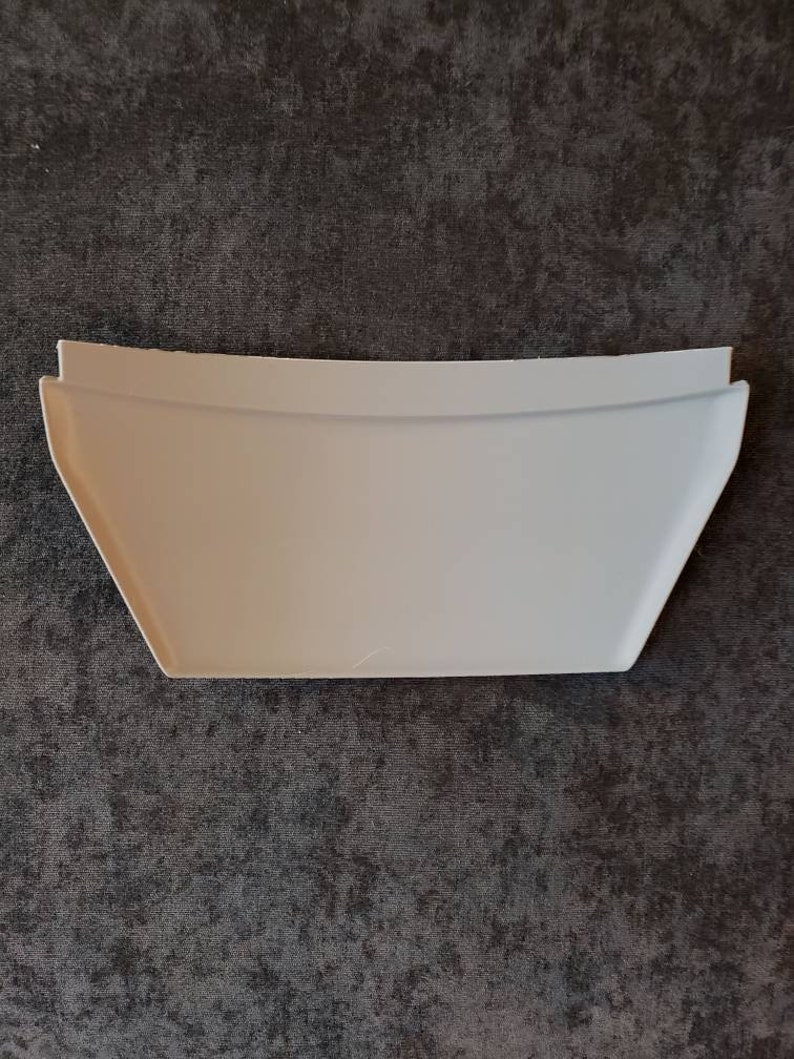 Puede incluir: Un revestimiento de estante de pl&aacute;stico blanco con un borde curvo. El revestimiento est&aacute; dise&ntilde;ado para encajar en una esquina y evitar que los art&iacute;culos se deslicen.