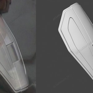 May include: A white, plastic, rectangular shield with a raised, curved design. The shield has a small, rectangular opening in the center.