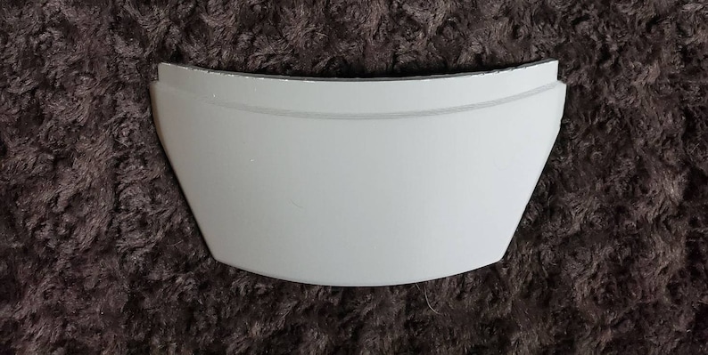 Puede incluir: Pieza curva de pl&aacute;stico blanco con una superficie lisa. Esta pieza probablemente forma parte de un objeto m&aacute;s grande.