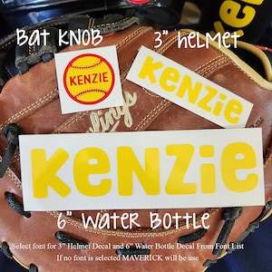 May include: A baseball glove holds three decals: a yellow and red softball bat knob sticker with "KENZIE", a yellow "Kenzie" sticker for a 3" helmet, and a larger yellow "Kenzie" sticker for a 6" water bottle. The text "Select font..." is also visible.
