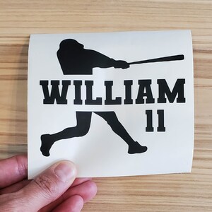 May include: A white sticker featuring a black silhouette of a baseball player mid-swing. The name "WILLIAM" is printed in bold, black capital letters above the player, with the number "11" below.