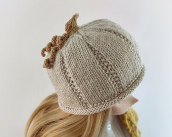 Peut inclure: Un chapeau en tricot beige avec une tige de citrouille en feutre marron sur le dessus. Le chapeau est porté par une poupée aux longs cheveux blonds et qui porte un cardigan jaune et une blouse blanche.