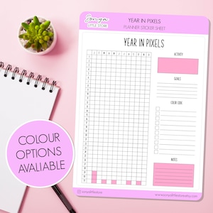以下が含まれることがあります： 「Year in Pixels」の文字と、アクティビティを追跡するためのグリッドが記載されたプランナーステッカーシート。目標、カラーコード、メモのセクションが含まれています。小さな多肉植物とスパイラルノートも表示されています。