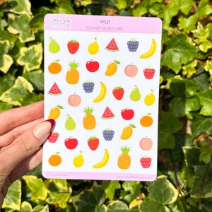 May include: A sheet of fruit planner stickers with a variety of fruits including watermelon, pineapple, mango, banana, strawberries, apples, pears, lemons, oranges, and raspberries. The sticker sheet is pink and white with the text "Fruit Planner Sticker Sheet" and "Sonya Little Store" printed on it.