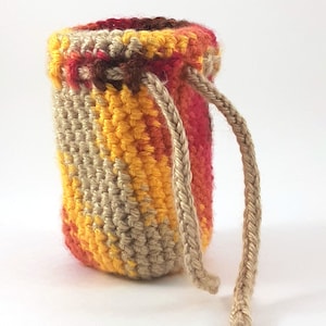 Puede incluir: Una pequeña bolsa de cordón de ganchillo con un patrón de rayas marrones, amarillas y rojas. La bolsa tiene un largo cordón marrón.