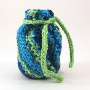 Puede incluir: Una pequeña bolsa de cordón de ganchillo con un cordón verde. La bolsa está hecha con hilo azul, verde y turquesa.