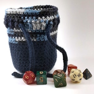 Puede incluir: Una bolsa de dados de crochet azul con cierre de cordón, y seis dados de varios colores, incluyendo rojo, verde y crema, con números negros.