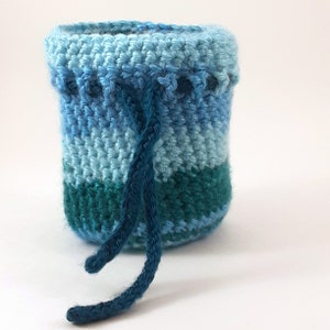 Puede incluir: Una pequeña bolsa de cordón de ganchillo con un patrón de degradado azul y verde. La bolsa está hecha con un hilo suave y tiene un diseño sencillo.