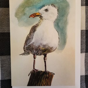 May include: Watercolor painting of a white seagull with a yellow beak standing on a wooden post against a blue and green watercolor background.