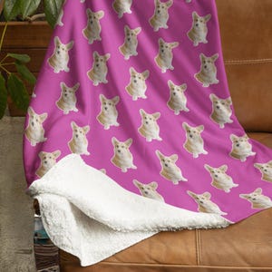 Op de afbeelding: Een roze fleece deken met een herhalend patroon van een corgi hondenkop. De deken heeft een witte sherpa voering.