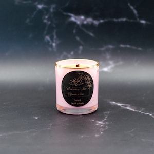 May include: A light pink candle in a glass jar with a gold-toned rim. A circular black label on the front features the text MJC, an orchid illustration, and the words Beeswax, Not Yours, Inc. along with the text Natural BeesWax Candle.