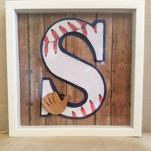 May include: A white letter S with a baseball stitching pattern, a brown baseball glove, and a woodgrain background in a white frame.