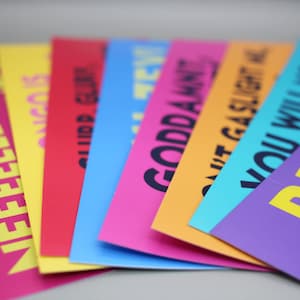 Könnte beinhalten: Eine Sammlung rechteckiger Papierkarten, die fächerförmig angeordnet sind. Jede Karte hat eine andere einfarbige Hintergrundfarbe wie Pink, Gelb, Rot, Blau, Orange und Lila, mit fett gedrucktem schwarzem oder gelbem Text auf jeder Karte.