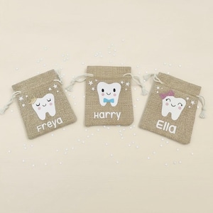 Op de afbeelding: Drie kleine, beige jute tandfee cadeauzakjes. Elke tas heeft een lachende tandafbeelding met een naam eronder: Freya, Harry en Ella. De tassen hebben witte trekkoorden en steraccenten. Een schattig en grillig ontwerp.