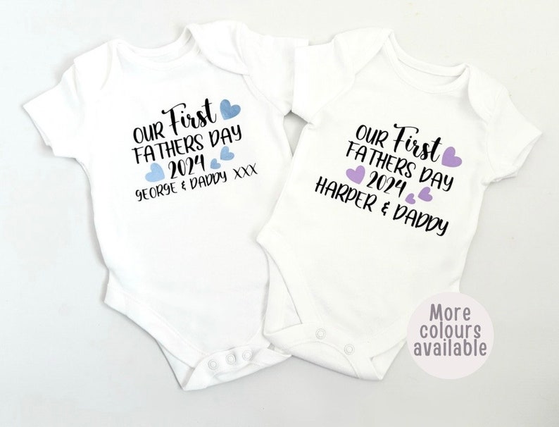 May include: Two white baby onesies with the text "Our First Father's Day 2024" and the names "George & Daddy" and "Harper & Daddy" printed on them. The onesies have blue and purple hearts printed on them.