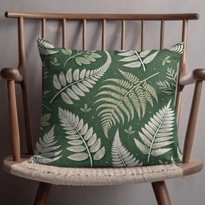 May include: A green throw pillow with a white fern pattern. The pillow is sitting on a wooden chair with a woven seat.