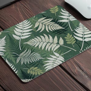 May include: A green mouse pad with a white fern pattern. The ferns are arranged in a repeating pattern on a dark green background.
