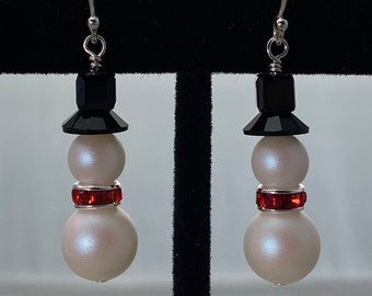 May include: A pair of silver snowman earrings with black and white beads and a red rhinestone accent.