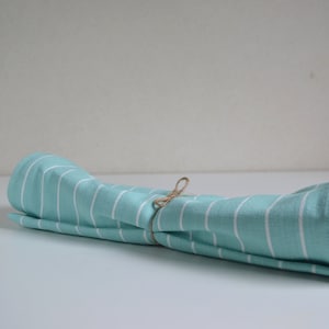 Op de afbeelding: Een opgerolde tealblauwe en wit gestreepte keukendoek, vastgebonden met touw.