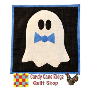 Könnte beinhalten: Ein weißer Geist mit einer blauen Schleife auf schwarzem Hintergrund mit blauem Rand. Der Geist hat zwei schwarze Augen. Der Text "Candy Cane Ridge Quilt Shop" befindet sich unter dem Bild.