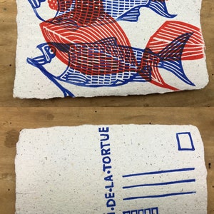 Puede incluir: Una postal con una impresi&oacute;n azul y roja de dos peces sobre un fondo blanco. El texto "LE CRI DE LA TORTUE" est&aacute; impreso en azul en el lado derecho de la postal.