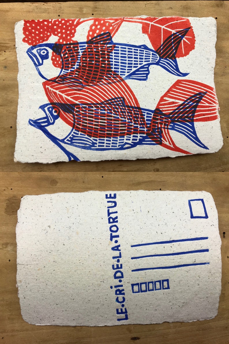 Puede incluir: Una postal con una impresi&oacute;n azul y roja de dos peces sobre un fondo blanco. El texto "LE CRI DE LA TORTUE" est&aacute; impreso en azul en el lado derecho de la postal.