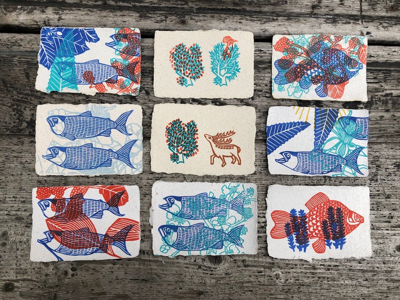 Puede incluir: Nueve tarjetas peque&ntilde;as con dise&ntilde;os impresos a mano. Las tarjetas presentan peces azules y rojos, un ciervo y patrones florales.