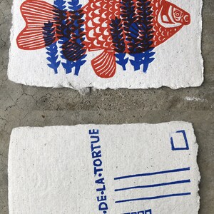 Puede incluir: Una postal con una ilustraci&oacute;n de un pez rojo y azul y el texto "LE CRI DE LA TORTUE" impreso en azul en el frente.
