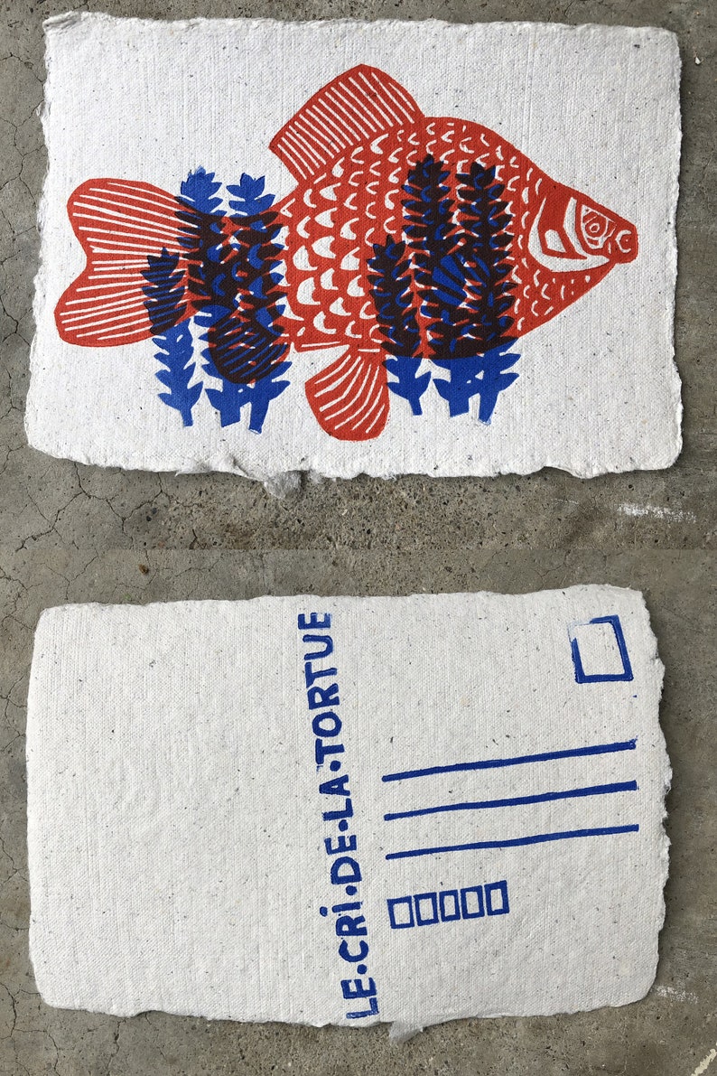 Puede incluir: Una postal con una ilustraci&oacute;n de un pez rojo y azul y el texto "LE CRI DE LA TORTUE" impreso en azul en el frente.