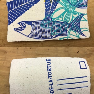 Puede incluir: Una postal azul y verde con un dise&ntilde;o de pez y flores. El texto "LE CRI DE LA TORTUE" est&aacute; impreso en la parte posterior.