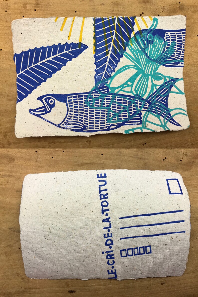 Puede incluir: Una postal azul y verde con un dise&ntilde;o de pez y flores. El texto "LE CRI DE LA TORTUE" est&aacute; impreso en la parte posterior.